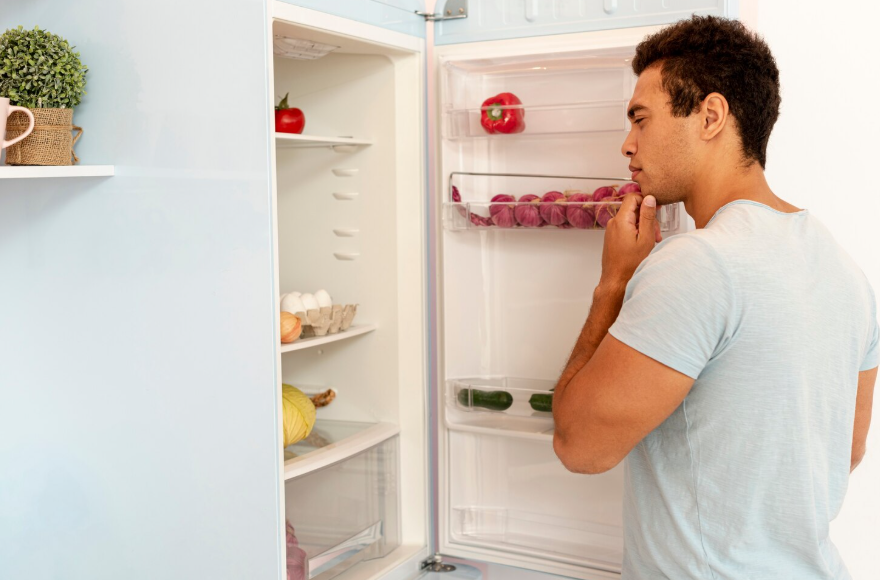 Person checking refrigerator contents before creating grocery list to reduce food waste